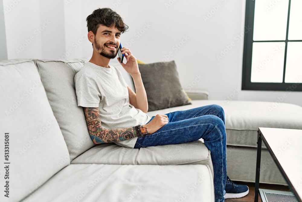 Young hispanic man using smartphone sitting on the sofa at home. Young hispanic man using smartphone sitting on the sofa at home.