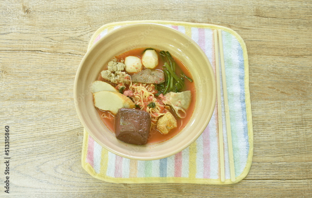 Chinese yellow egg noodles with fish ball and chop pork in spicy red tom yum soup on bowl Chinese yellow egg noodles with fish ball and chop pork in spicy red tom yum soup on bowl