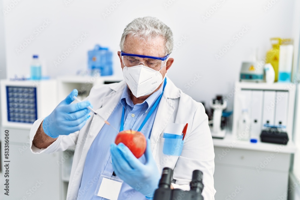 Middle age grey-haired man wearing scientist uniform holding syringe and apple at laboratory Middle age grey-haired man wearing scientist uniform holding syringe and apple at laboratory