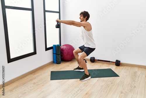 Young hispanic man smiling confident training using kettlebell at sport center