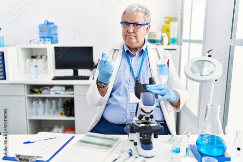 Senior caucasian man working at scientist laboratory doing money gesture with hands, asking for salary payment, millionaire business