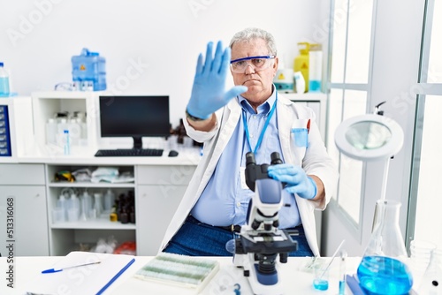 Senior caucasian man working at scientist laboratory doing stop sing with palm of the hand. warning expression with negative and serious gesture on the face.