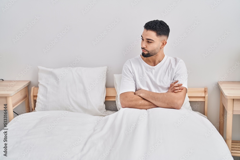 Young arab man sitting on bed with angry expression and arms crossed gesture at bedroom Young arab man sitting on bed with angry expression and arms crossed gesture at bedroom