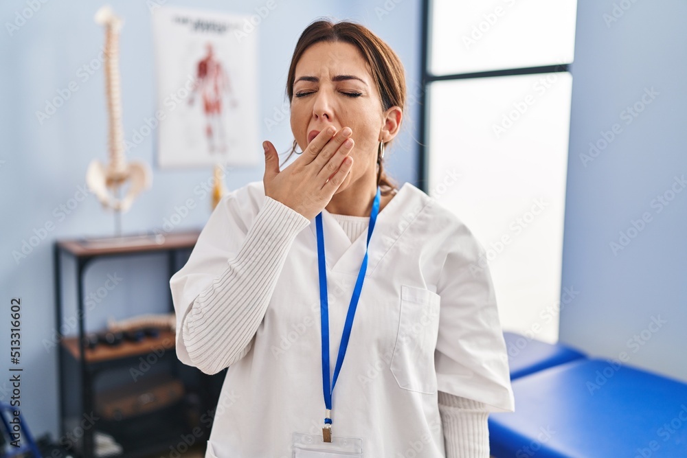 Young brunette woman working at pain recovery clinic bored yawning tired covering mouth with hand. restless and sleepiness. Young brunette woman working at pain recovery clinic bored yawning tired covering mouth with hand. restless and sleepiness.