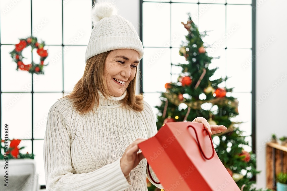Middle age caucasian woman smiling confident opening christmas gift bag at home