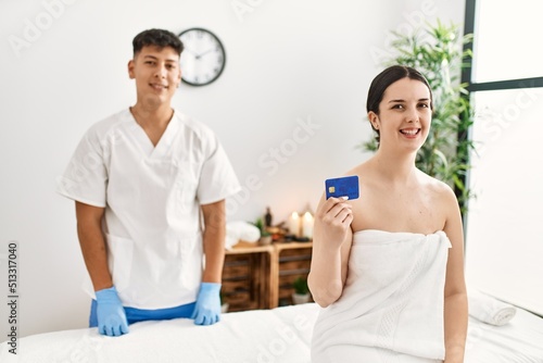 Woman smiling happy waiting to recive massage holding credit card at beauty center. photo