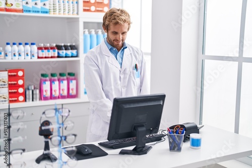 Young man pharmacist using computer working at pharmacy