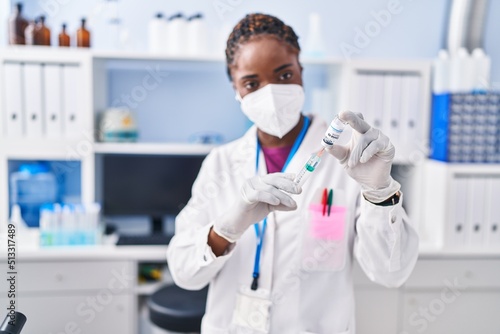 African american woman wearing scientist uniform and medical mask holding covid-19 vaccine at laboratory