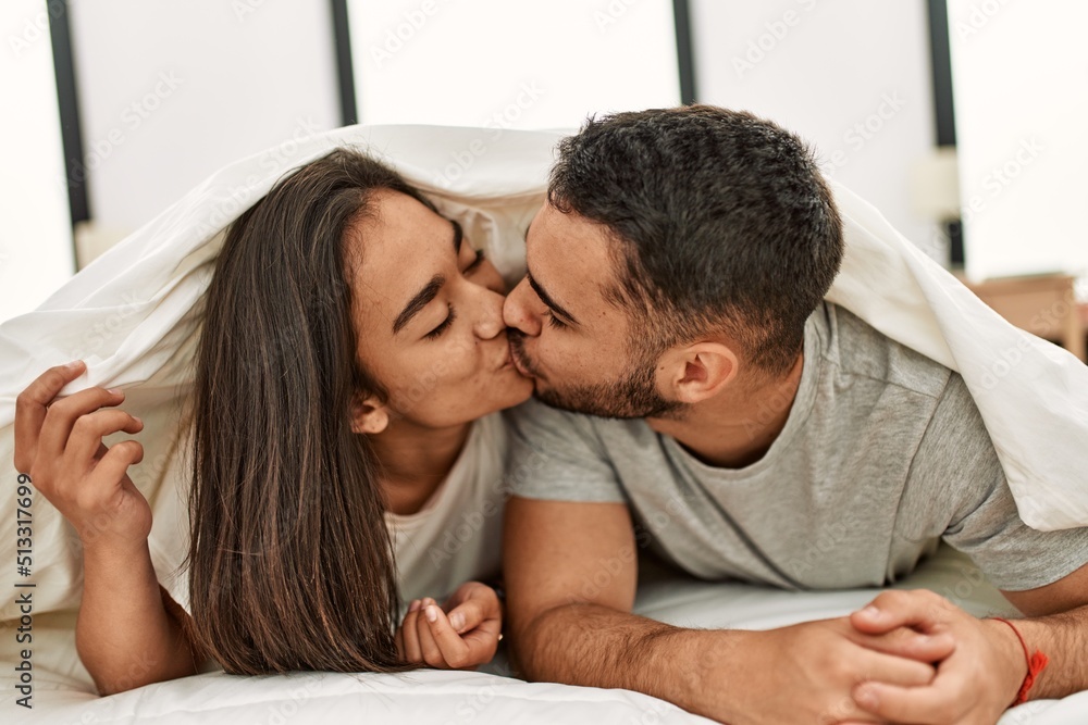 Young latin couple kissing and covering with bed sheet lying on the bed. Young latin couple kissing and covering with bed sheet lying on the bed.