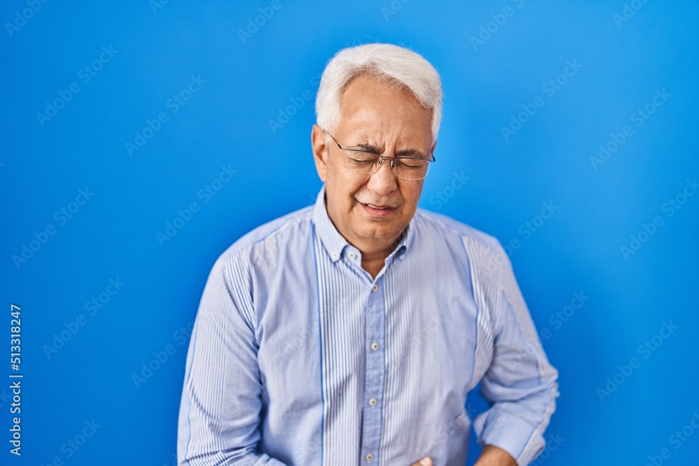Hispanic senior man wearing glasses with hand on stomach because indigestion, painful illness feeling unwell. ache concept. Hispanic senior man wearing glasses with hand on stomach because indigestion, painful illness feeling unwell. ache concept.