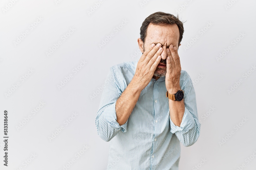 Middle age hispanic man with beard standing over isolated background rubbing eyes for fatigue and headache, sleepy and tired expression. vision problem Middle age hispanic man with beard standing over isolated background rubbing eyes for fatigue and headache, sleepy and tired expression. vision problem