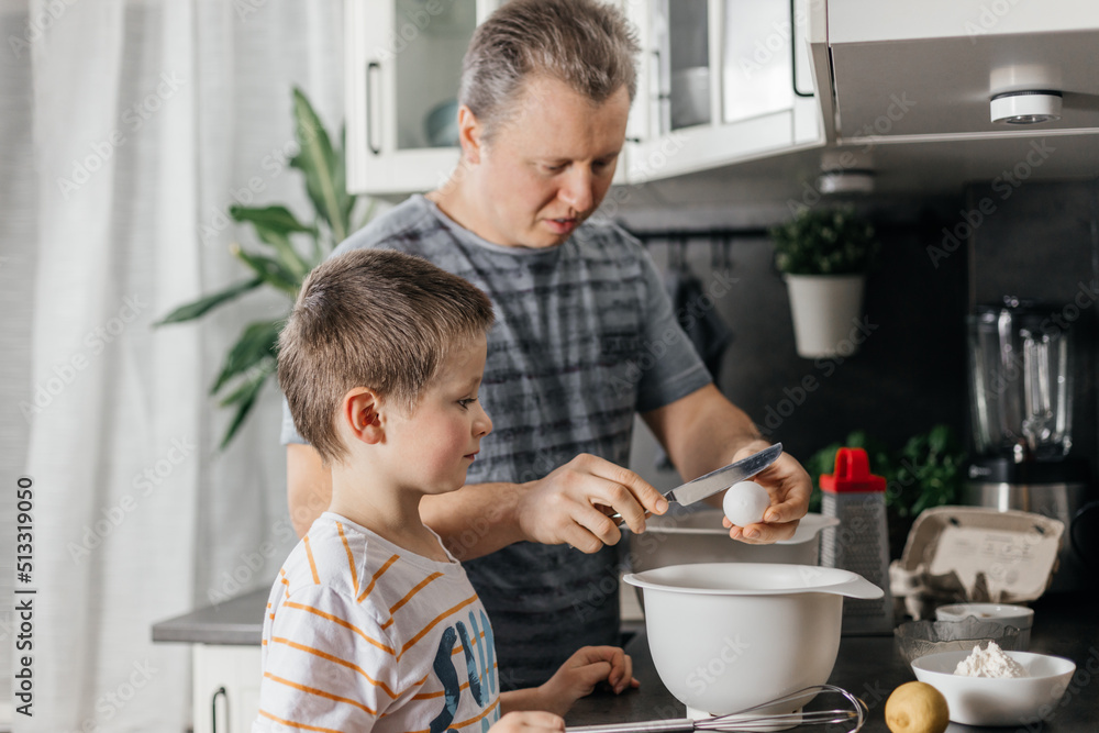 Caring dad cooks dough with his son in the kitchen. Cooking with children. Children are little helpers. Caring dad cooks dough with his son in the kitchen. Cooking with children. Children are little helpers.