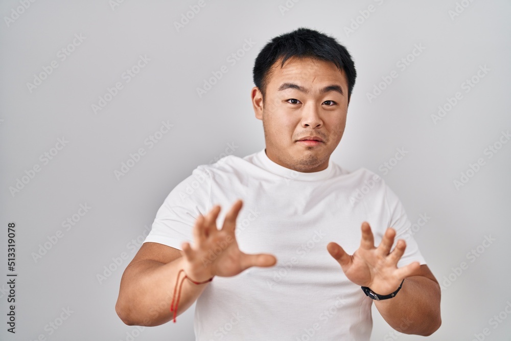 Young chinese man standing over white background afraid and terrified with fear expression stop gesture with hands, shouting in shock. panic concept. Young chinese man standing over white background afraid and terrified with fear expression stop gesture with hands, shouting in shock. panic concept.