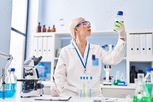 Young blonde woman wearing scientist uniform holding bottle at laboratory