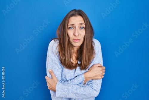 Fotografi Young woman standing over blue background shaking and freezing for winter cold w