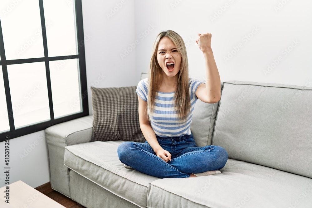 Asian young woman sitting on the sofa at home angry and mad raising ...