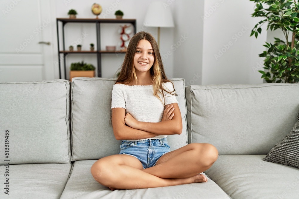 Young brunette teenager sitting on the sofa at home happy face smiling with crossed arms looking at the camera. positive person. Young brunette teenager sitting on the sofa at home happy face smiling with crossed arms looking at the camera. positive person.