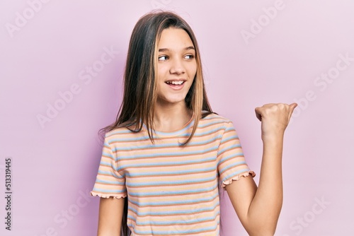 Young brunette girl wearing casual striped t shirt pointing thumb up to the side smiling happy with open mouth © Krakenimages.com