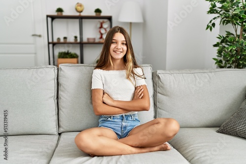 Young brunette teenager sitting on the sofa at home happy face smiling with crossed arms looking at the camera. positive person.