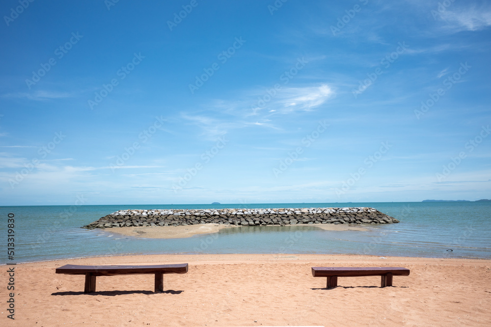 Outdoor sunny view of empty wooden bench on a beach against sea and blue sky. 