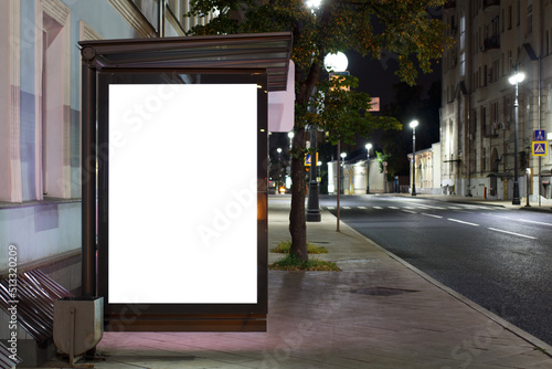 Empty billboard at the bus stop, night city lights. Cozy well-lit street. Mock-up.