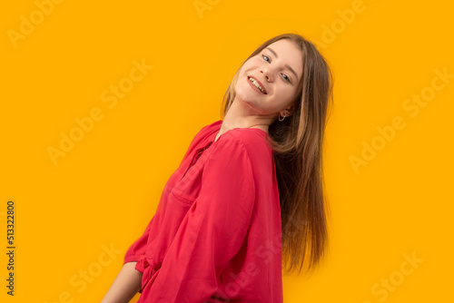 Portrait of young girl laughing and looking into camera. Young woman in red shirt on an yellow background.