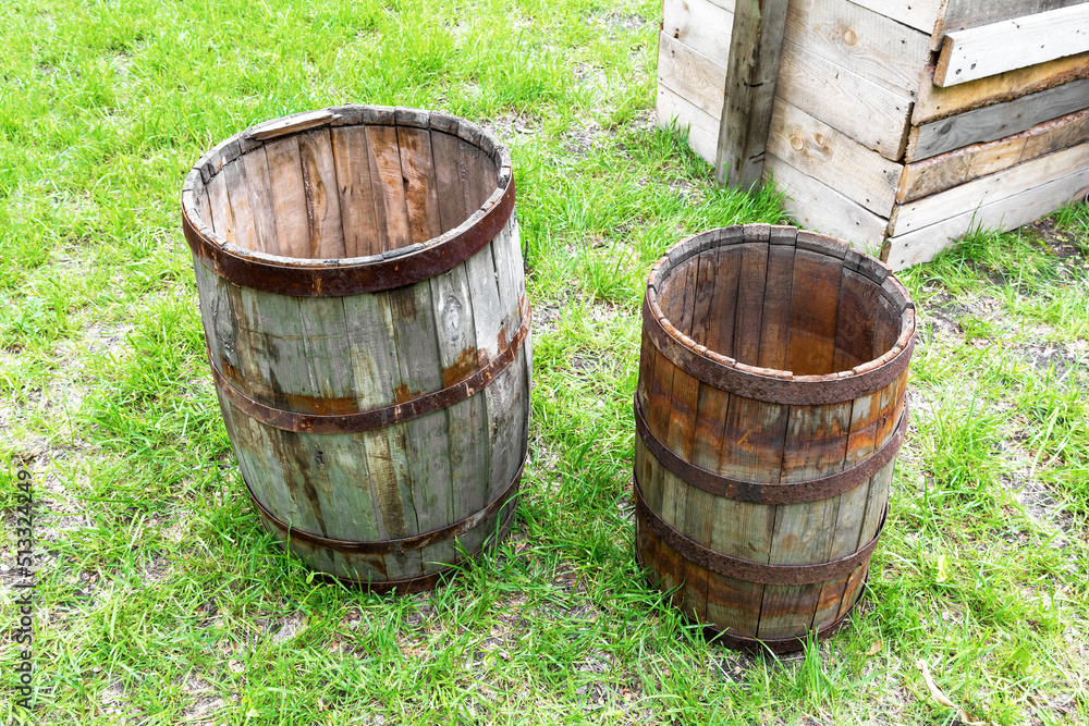 Old wooden barrels stand on the grass in the backyard in the village. Texture of weathered wood Old wooden barrels stand on the grass in the backyard in the village. Texture of weathered wood