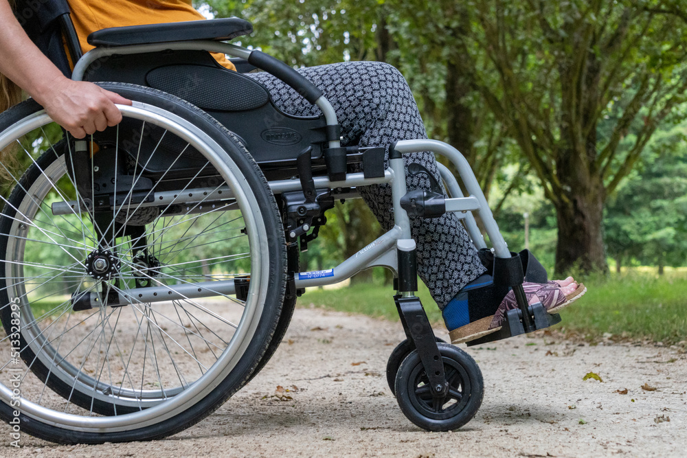 Fototapeta premium Close-up of a wheelchair in profile, a young woman sitting on it, in the middle of nature