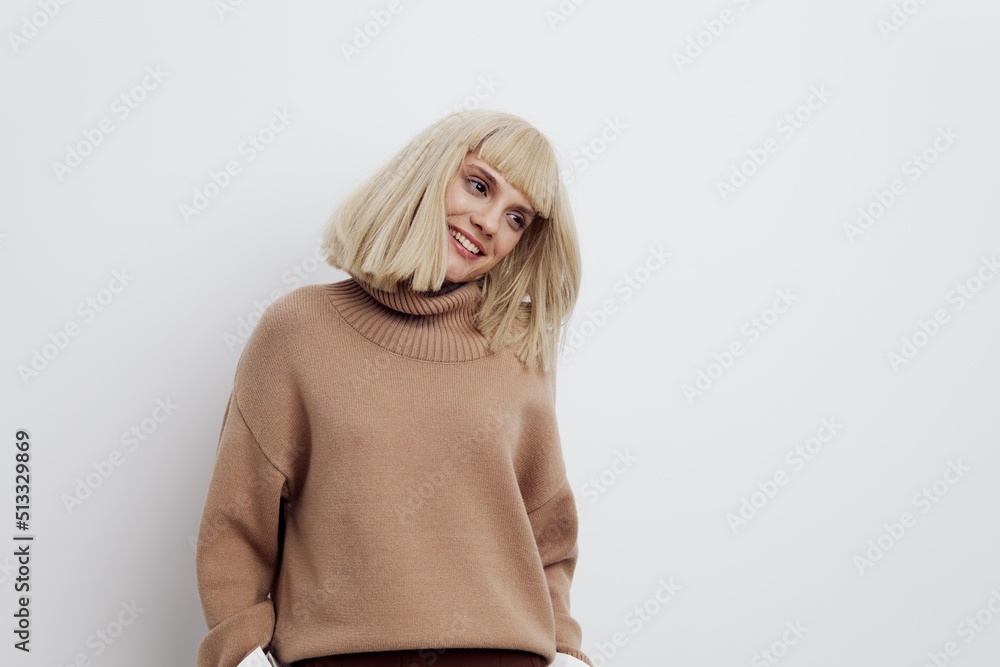 an attractive woman stands on a light background in a sweater and shirt, happily turns her head waving her hair an attractive woman stands on a light background in a sweater and shirt, happily turns her head waving her hair