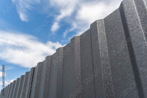 Iron fence and blue sky. A fence from a profiled sheet against the sky with white clouds.
