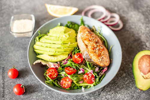 grilled salmon steak and fresh green vegetable tomato salad with lettuce and avocado on stone background