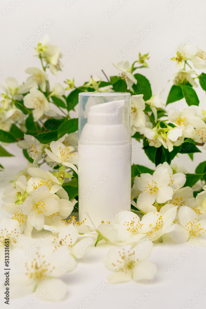 A white cosmetic jar with a dispenser against the background of fragrant white flowers and green leaves of an ornamental shrub. Jasmine or Philadelphus. Body or face cream mockup. A white cosmetic jar with a dispenser against the background of fragrant white flowers and green leaves of an ornamental shrub. Jasmine or Philadelphus. Body or face cream mockup.