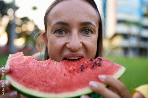 Close up of excited young girl in summer spending time at the park, biting slice of a watermelon. High quality photo