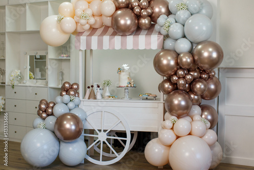 Street vending cart against the backdrop of an indoor cabinet  decorated with brown  beige and gray helium balloons  flowers. On the cart is a cake with the inscription Happy Birthday  ice cream.