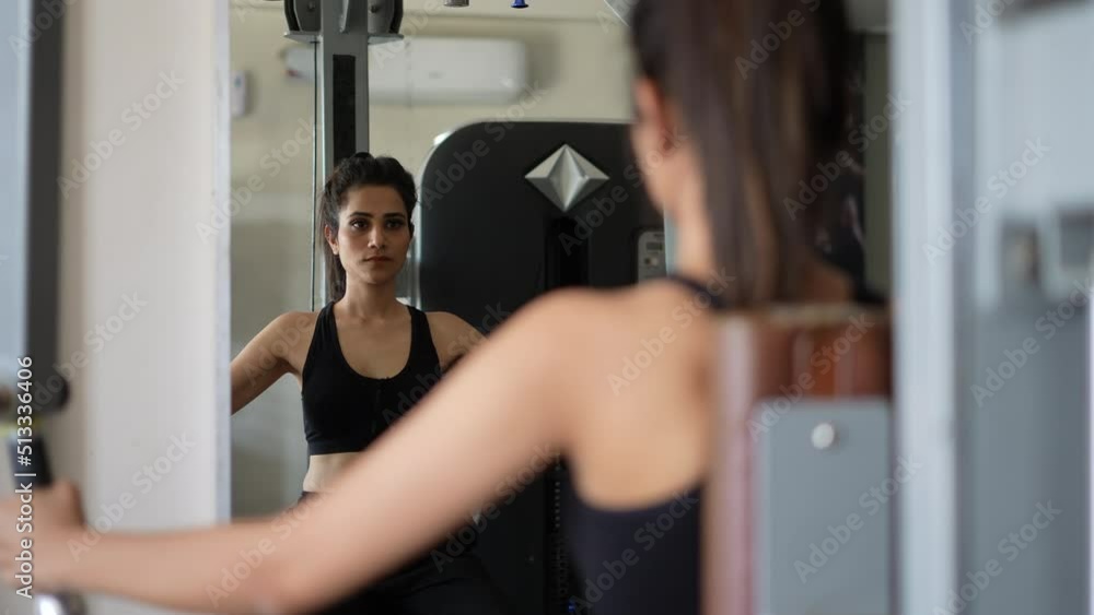 A young Indian girl doing musculer execrise front on glass.female fitness concept.Indian girl execrise with machines in the gym. A young Indian girl doing musculer execrise front on glass.female fitness concept.Indian girl execrise with machines in the gym.