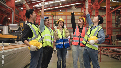 Group of Asian engineers and workers standing smiling wears safety helmet with joined stacking hand and hand up after working success together in factory.
