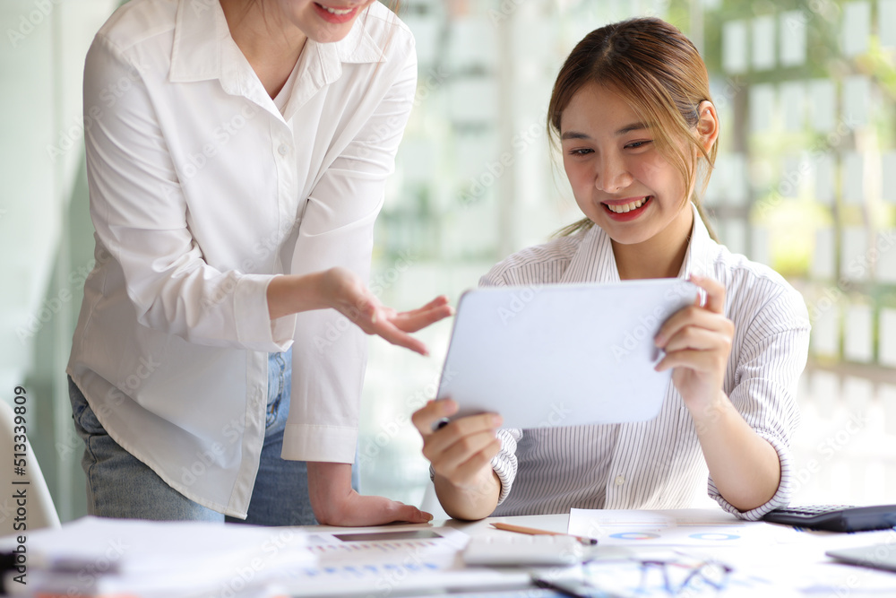 Businesswoman colleagues in the office discussing work and planning projects together on a tablet at their desk. Businesswoman colleagues in the office discussing work and planning projects together on a tablet at their desk.
