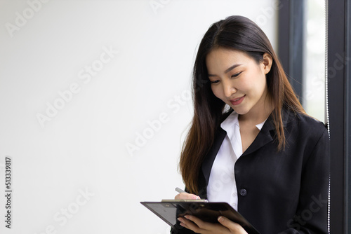 Young Asian businesswoman or office secretary standing holding papers and pens to write notes on paper.