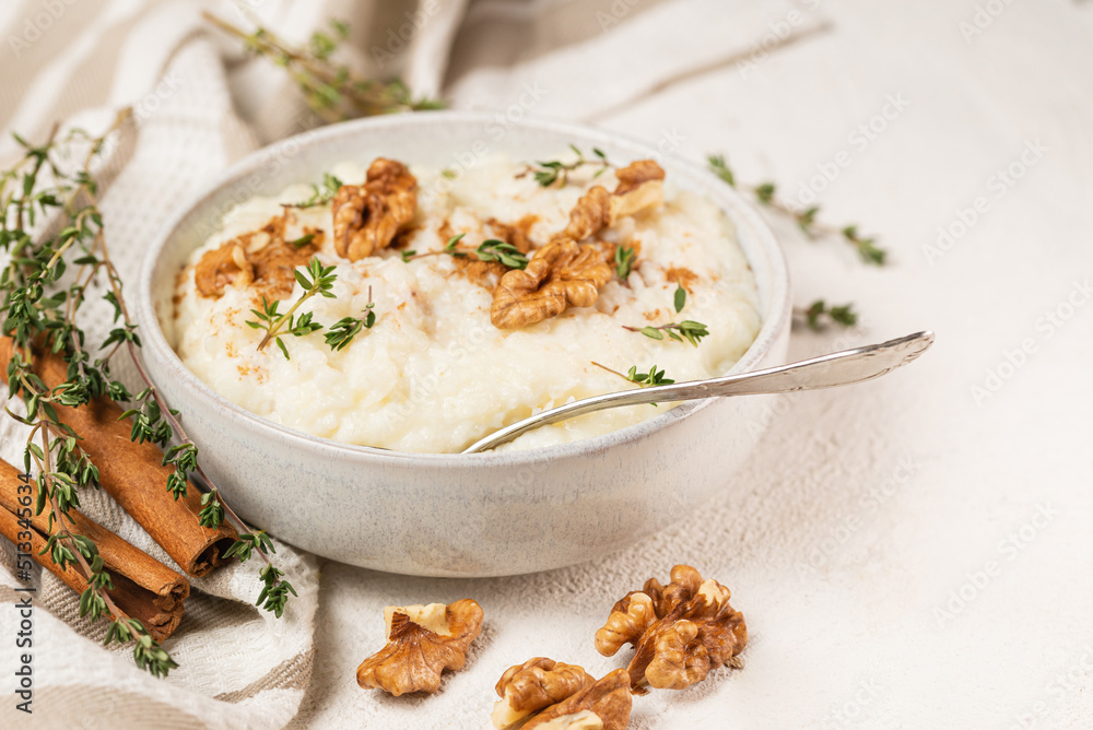 Focus selective photo of rice pudding finished with cinnamon powder, walnuts and thyme in white plate with teaspoon on striped napkin on light table