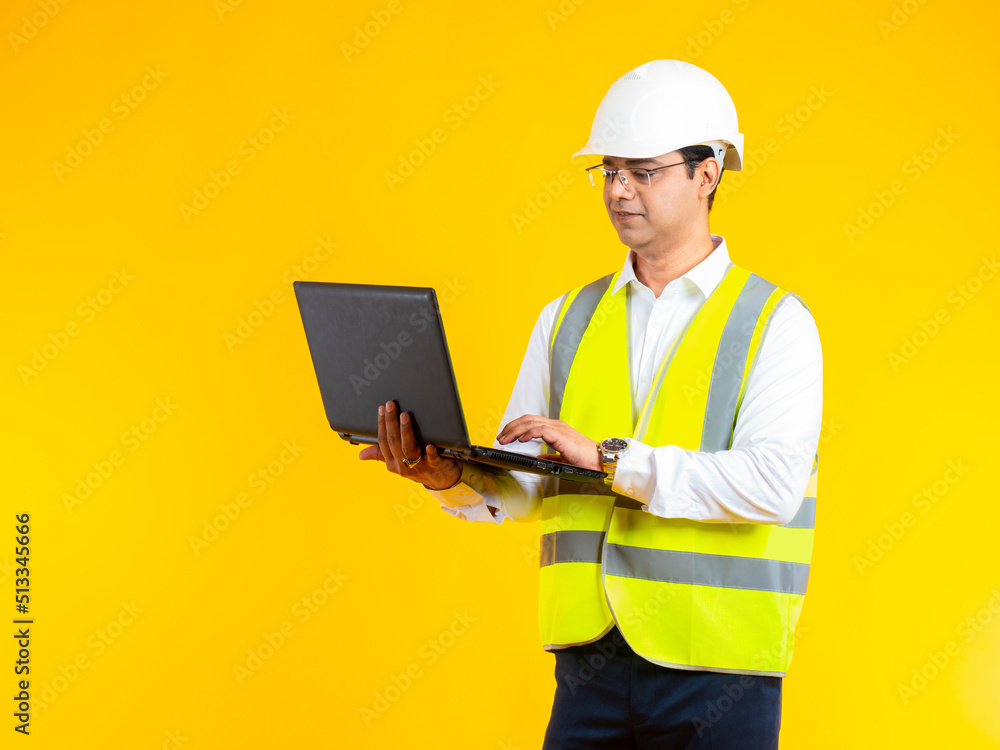 Man builder. Builder stands with laptop in his hands. Guy in construction uniform on yellow. Young engineer wearing reflective vest. Man is using laptop. Construction software concept. Builder career Man builder. Builder stands with laptop in his hands. Guy in construction uniform on yellow. Young engineer wearing reflective vest. Man is using laptop. Construction software concept. Builder career