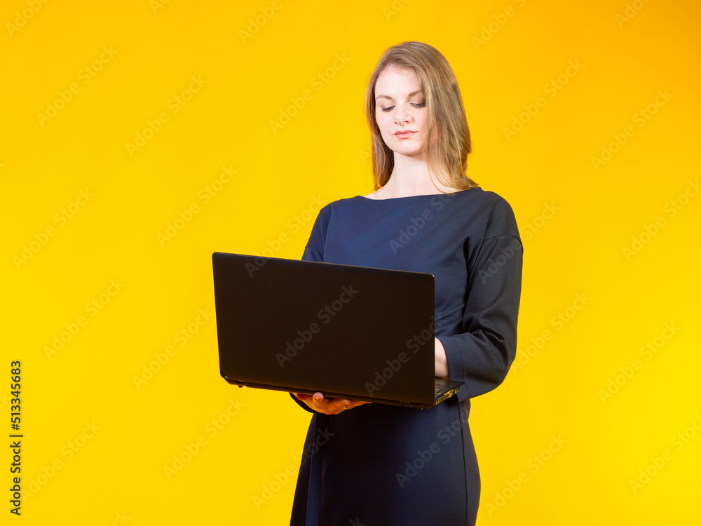Businesswoman with laptop. Woman is standing with laptop computer. Girl in long dress works with laptop. Lady use computer software. Internet surfing concept. Woman entrepreneur on yellow Businesswoman with laptop. Woman is standing with laptop computer. Girl in long dress works with laptop. Lady use computer software. Internet surfing concept. Woman entrepreneur on yellow