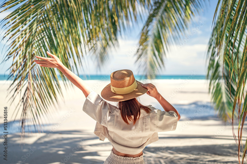 © oatawa - Summer beach vacation concept, Happy woman with hat relaxing at the seaside and looking away, in the summer against a backdrop of palm trees and sea beach.