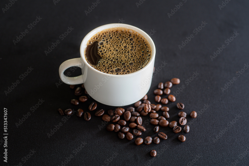 Cup full of coffee with bubbles and black coffee beans on black background. Cup full of coffee with bubbles and black coffee beans on black background.