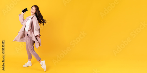 Smiling asian woman white shirt and blazer on yellow background holding smart phone
