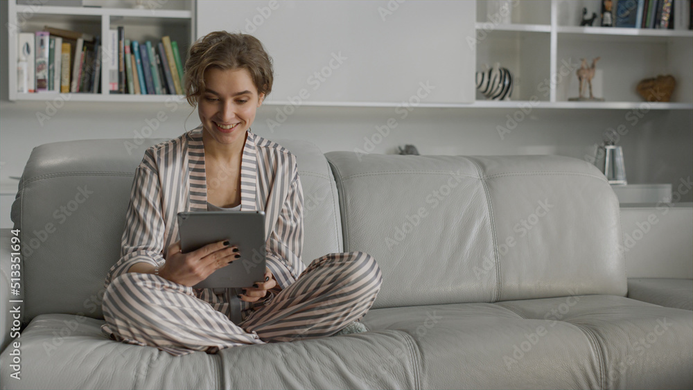 Fototapeta premium Student having online video conversation in living room. Smiling girl using pad 