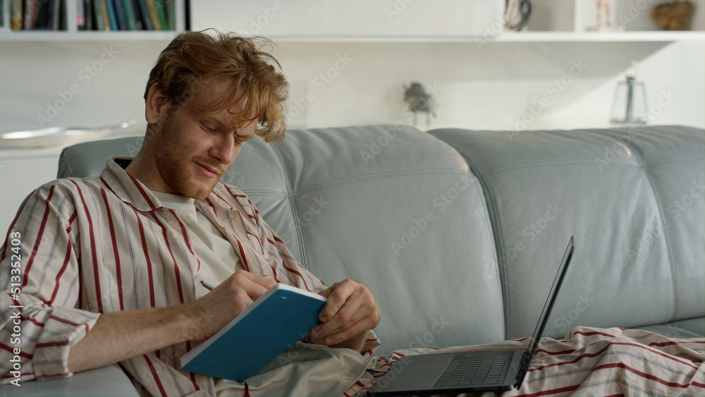 Smiling guy elearning home on weekend closeup. Ginger student work making notes Smiling guy elearning home on weekend closeup. Ginger student work making notes