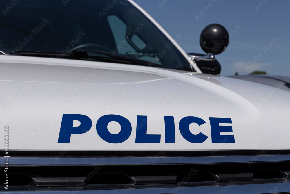POLICE printed on the front of a police car in blue text and a spotlight in the background. POLICE printed on the front of a police car in blue text and a spotlight in the background.