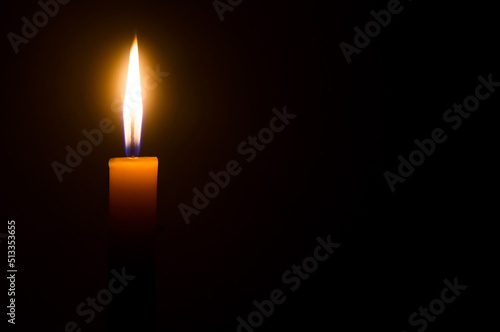 A single burning candle flame or light glowing on a yellow candle isolated on black or dark background on table in church for Christmas, funeral or memorial service