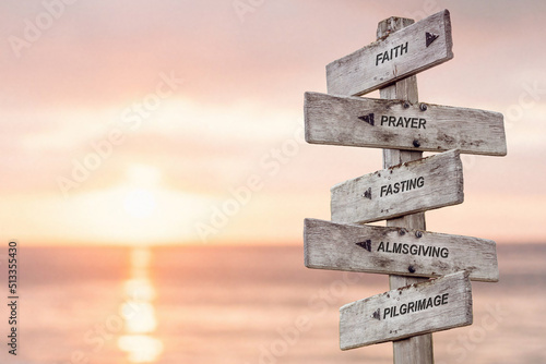 faith prayer fasting almsgiving pilgrimage text engraved on wooden signpost by the ocean during sunset. five pillars of islam.