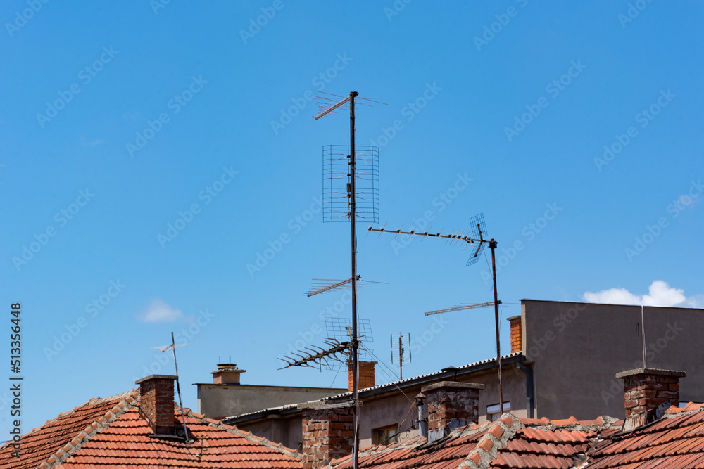 Many analog tv antennae over the red roof of houses and blue sky in the background on a summer day. The retro style of television signal. Copy space Many analog tv antennae over the red roof of houses and blue sky in the background on a summer day. The retro style of television signal. Copy space